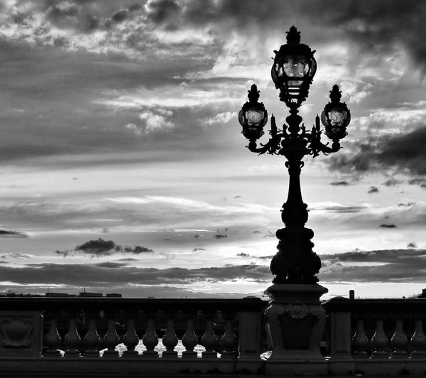 Silhouette old-fashioned street light on pont alexandre iii bridge against sky during sunset
