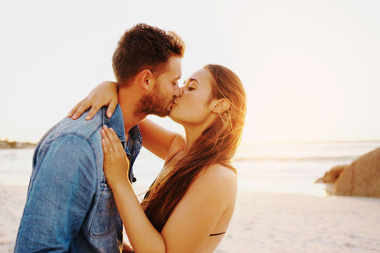 Young couple kissing at beach against sky