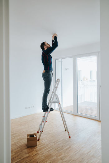 Full length of man standing on ladder at home