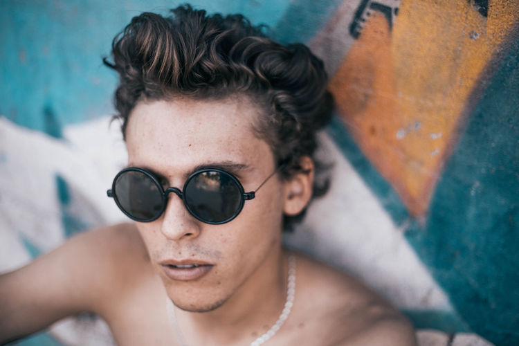 Close-up of shirtless young man wearing sunglasses against wall