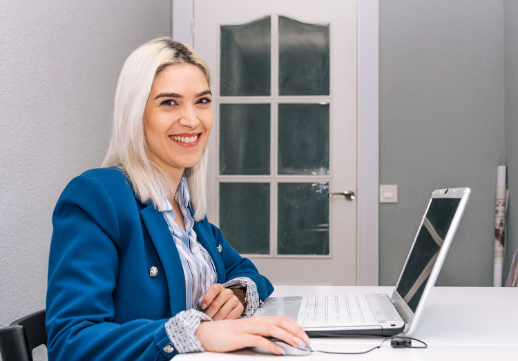Portrait of smiling businesswoman using laptop on desk in office