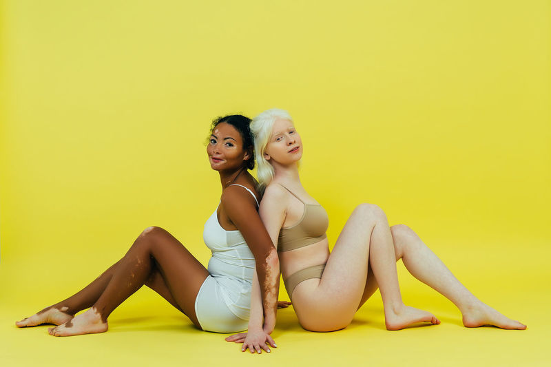 Side view of young women sitting against yellow background