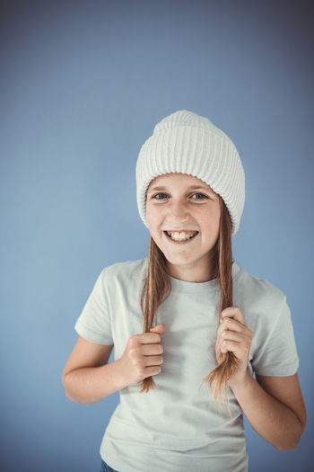 Portrait of smiling young woman wearing hat against blue background