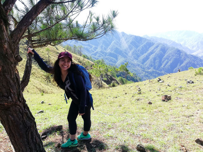 Happy young woman standing by tree against mountain