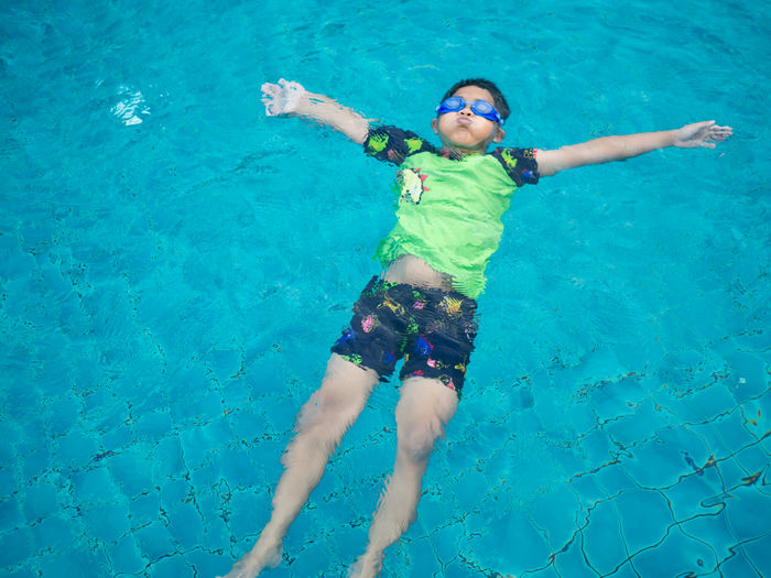 Boy wearing a swimsuit and glasses swimming in the middle of the pool with a blue water background