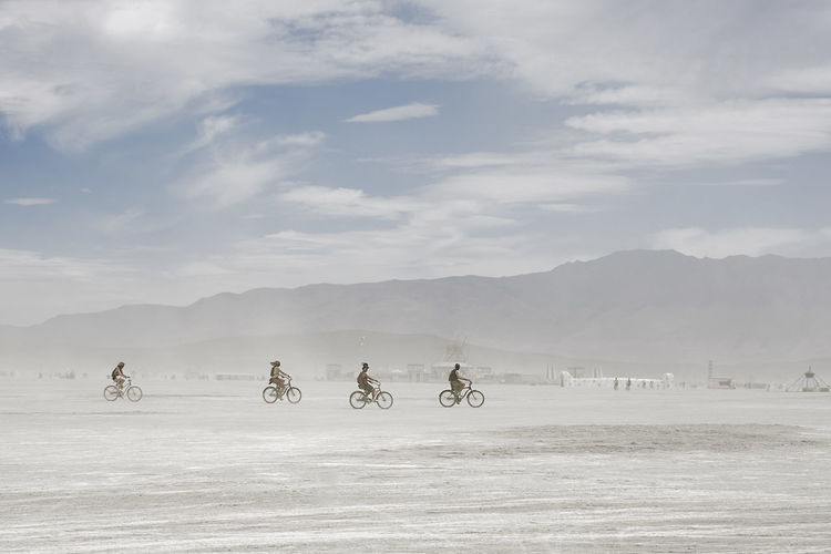 Distant view of cyclists riding bicycles at desert against sky