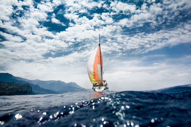 Yacht sailing on sea against cloudy sky
