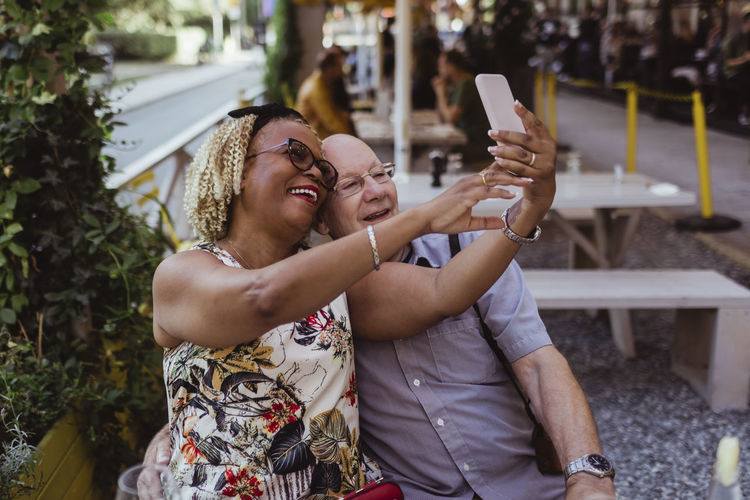 Cheerful heterosexual couple taking selfie on smart phone at cafe