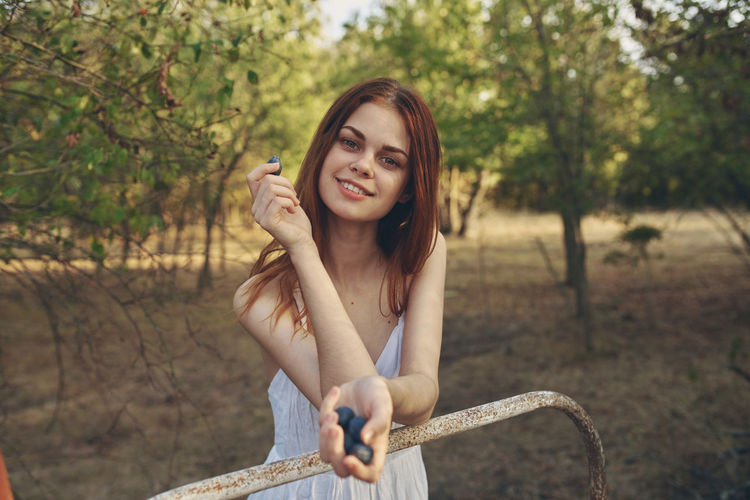 Portrait of smiling young woman holding plant against trees