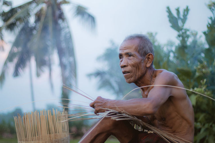 Shirtless man making wicker basket 