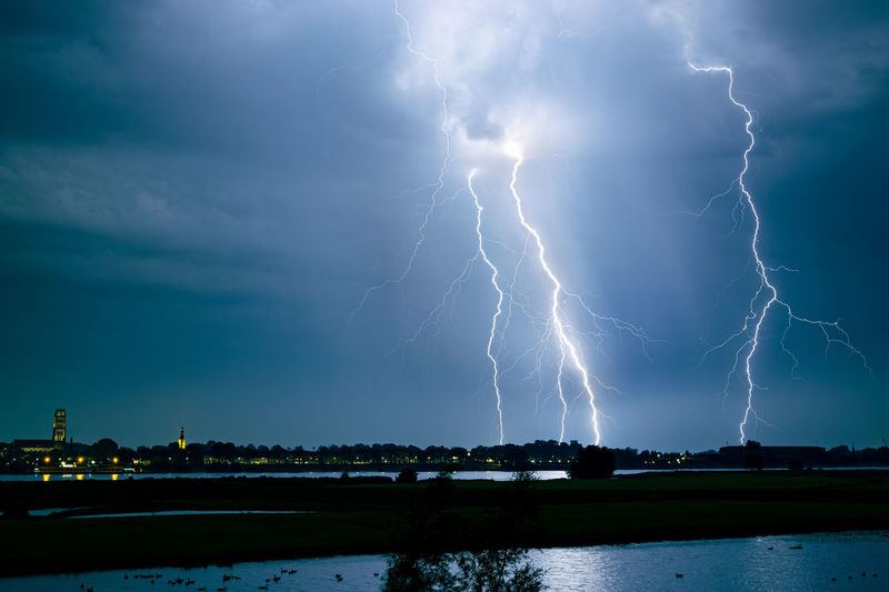 Lightning bolts strike at night near a town in a river landscape