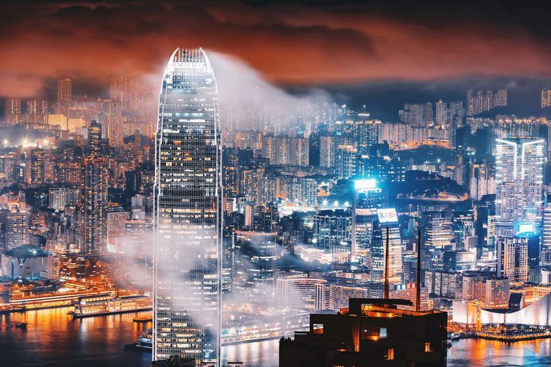 Illuminated cityscape against cloudy sky at night