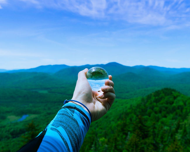 Cropped image of person holding crystal ball against mountains 