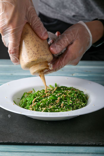 Close-up of person pouring green salad in plate on table