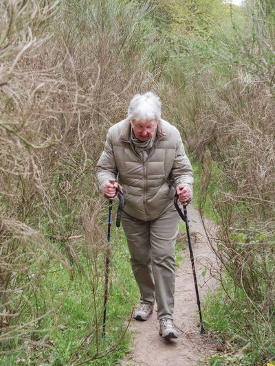 Woman on a narrow trail is hiking up hill with hiking sticks