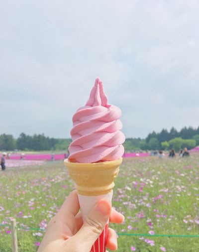 Hand holding ice cream cone against sky