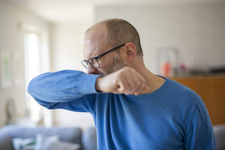 Man sneezes into his elbow