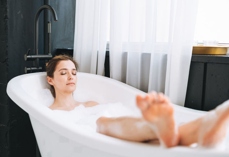 Young happy woman taking bath with foam at home, treat yourself