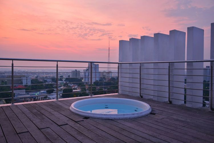 Swimming pool by building against sky during sunset