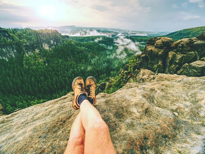 Hiker man take a rest on mountain peak. male legs on sharp summit and hiker enjoy spectacular view.
