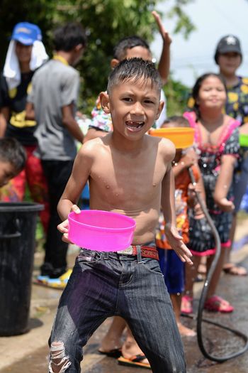 Portrait of boy holding container with people enjoying in background during songkran festival