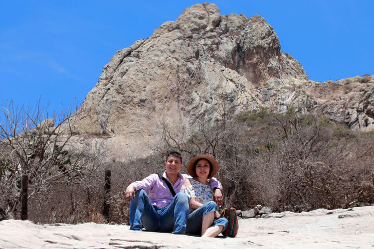 Portrait of man sitting on rock against mountain