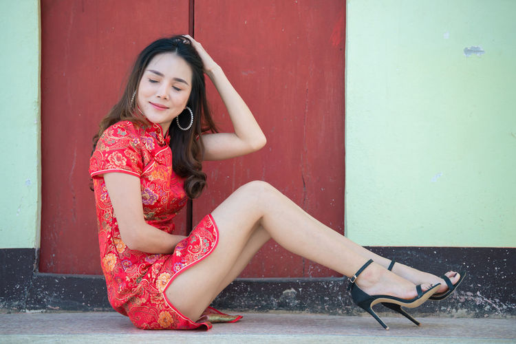 Portrait of a smiling young woman sitting against red wall