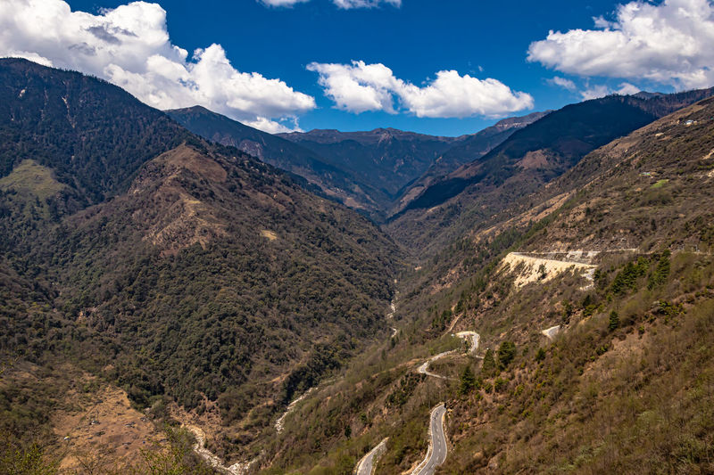 Mountain valley with curvy road and bright blue sky at sunny day from top