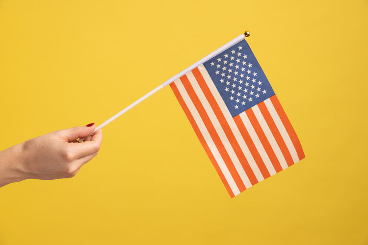 Cropped hand of woman holding flag against yellow background