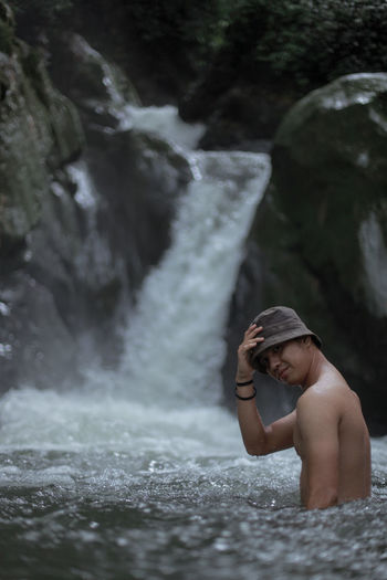 Portrait of young man in water against waterfall