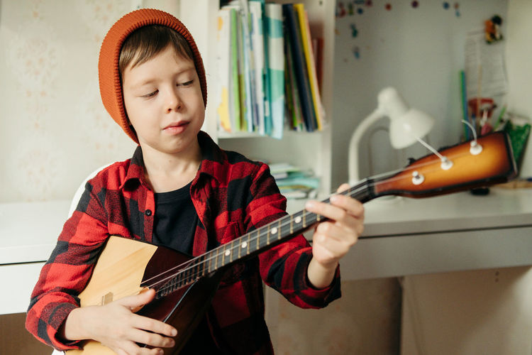 Boy in a red hat and a plaid shirt plays the balalaika. handsome boy holding his guitar. 