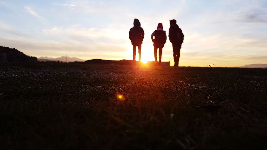 Silhouette family standing on land against sky during sunset