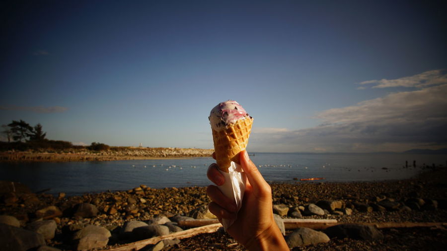 Woman holding ice-cream at beach against sky