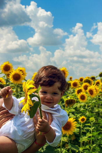 Mother holding boy with sunflower at field against sky