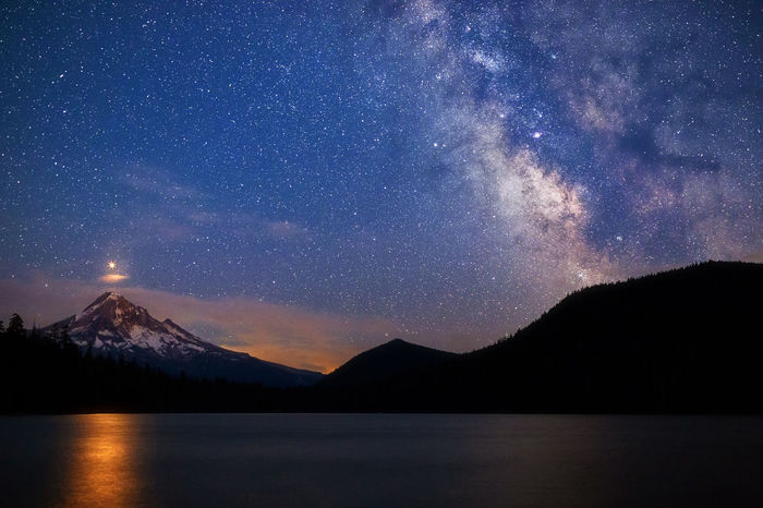 SCENIC VIEW OF LAKE AND MOUNTAINS AGAINST STAR FIELD AT NIGHT