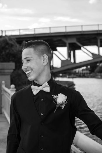 Smiling boy in suit standing on bridge against sky