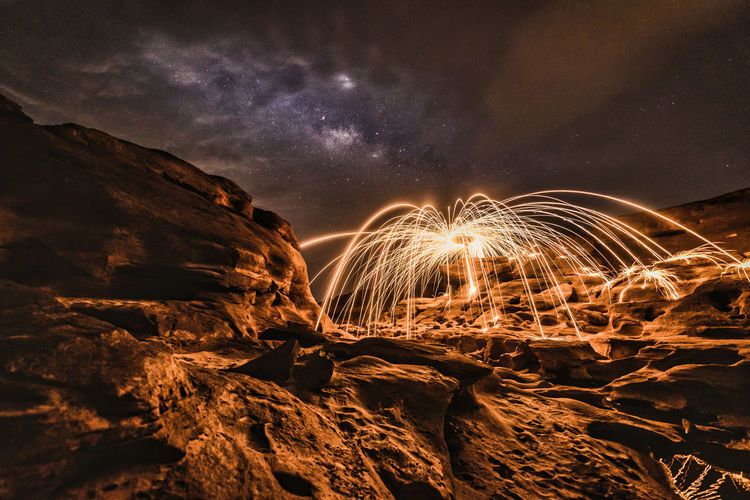 Light trails on rock formation against sky at night