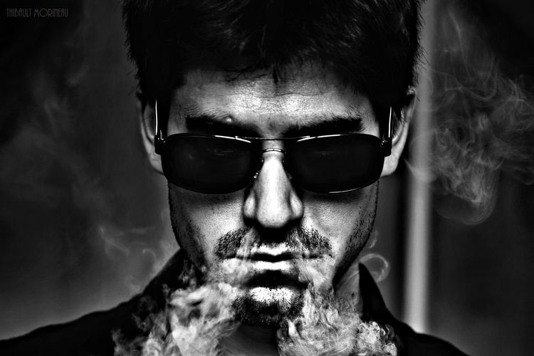 Close-up of young man wearing sunglasses while exhaling smoke through nose