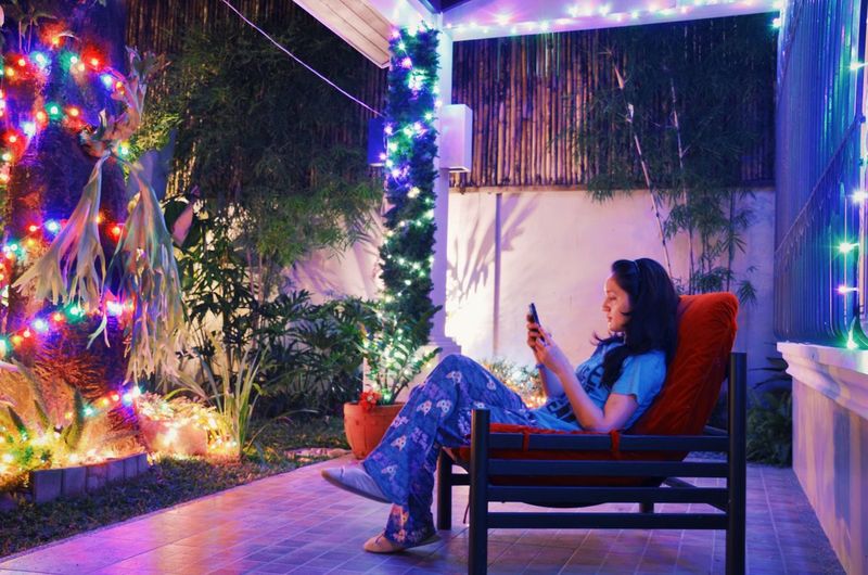Young woman sitting on chair while using smart phone at night