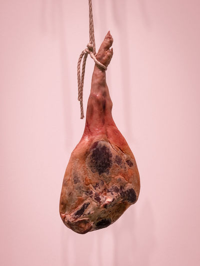 Close-up of pork leg hanging against pink background