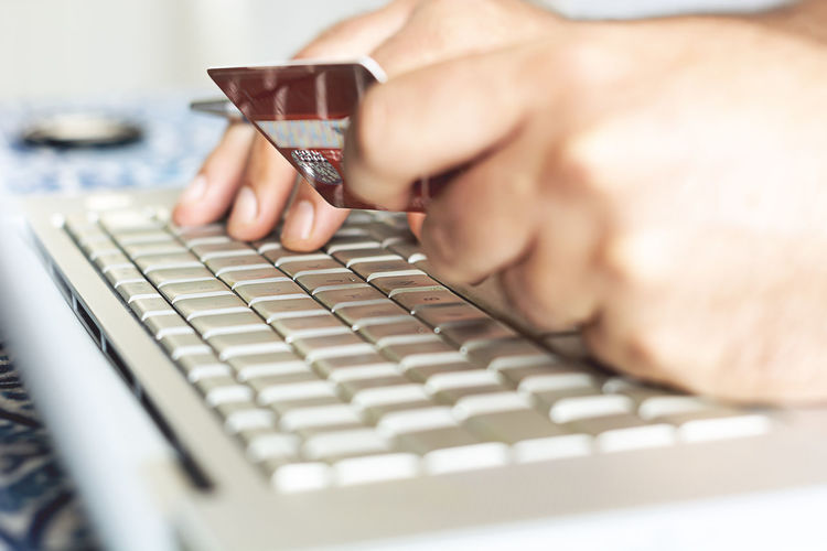 Cropped hand of man holding credit cart while using computer