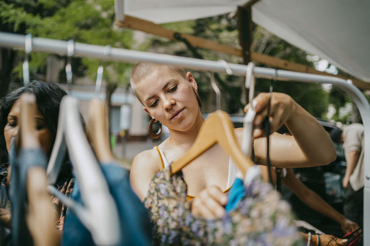 Young woman hanging dress on clothes rack at flea market