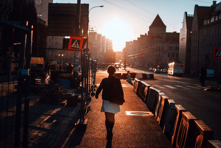 Rear view of woman walking by barricades on street during sunset