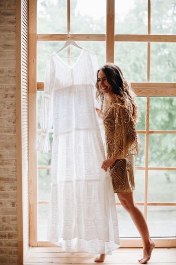 Woman holding wedding dress while standing against window