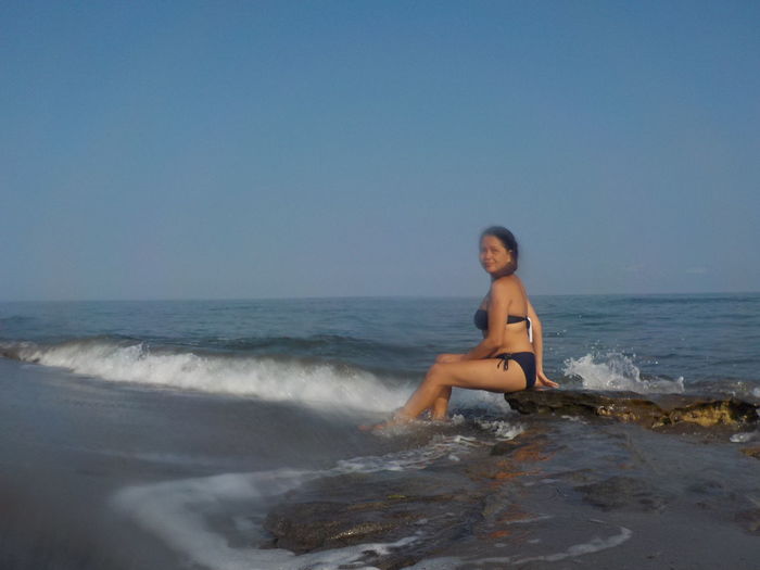 Young woman sitting on beach against clear sky