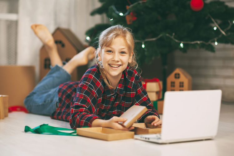 A happy little girl opens a gift under the christmas tree at home 