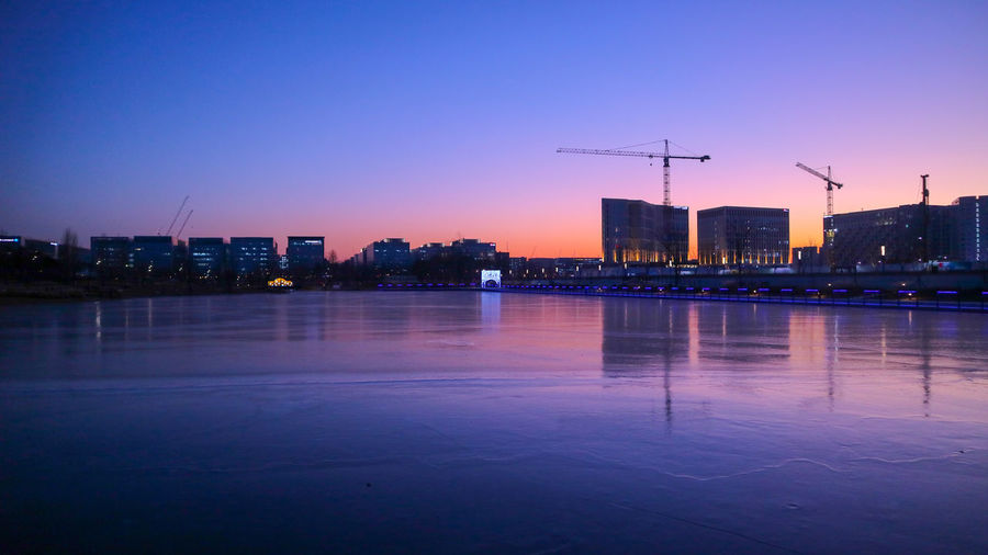 Illuminated buildings in city against clear sky at sunset