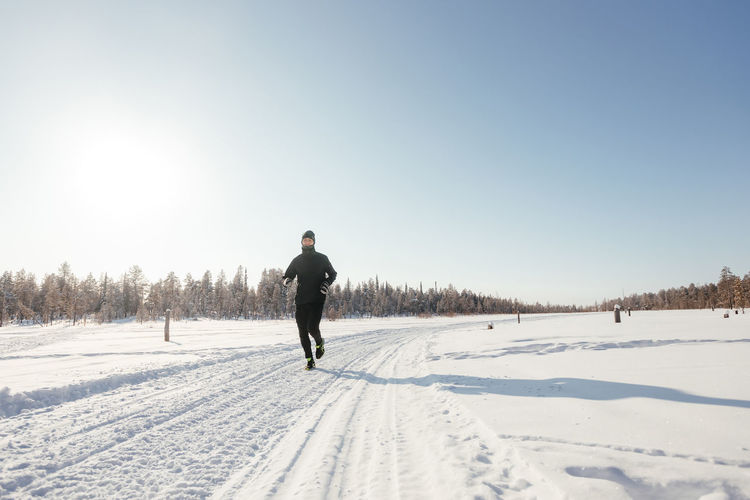 Full length of a happy middle-aged athlete running in nature on a snowy winter day. outdoor fitness
