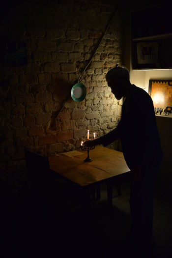 Side view of young man standing on table against illuminated wall