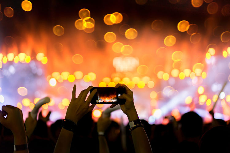 Cropped hands of person photographing with smart phone at music concert